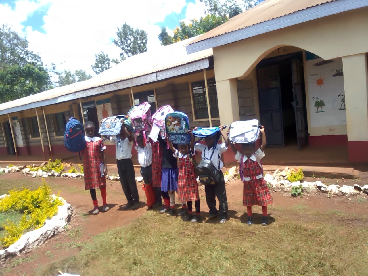 Pupils holding up new backpacks outside a classroom block